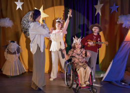 4 children on a stage with stars on their heads. One child is a wheelchair user.
