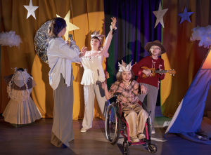 4 children on a stage with stars on their heads. One child is a wheelchair user. 