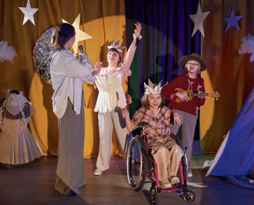 4 children on a stage with stars on their heads. One child is a wheelchair user.