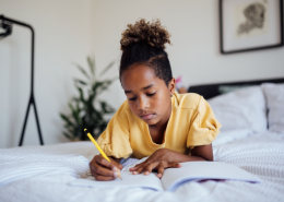 Child doing homework laid on their bed.