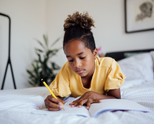 Child doing homework laid on their bed.