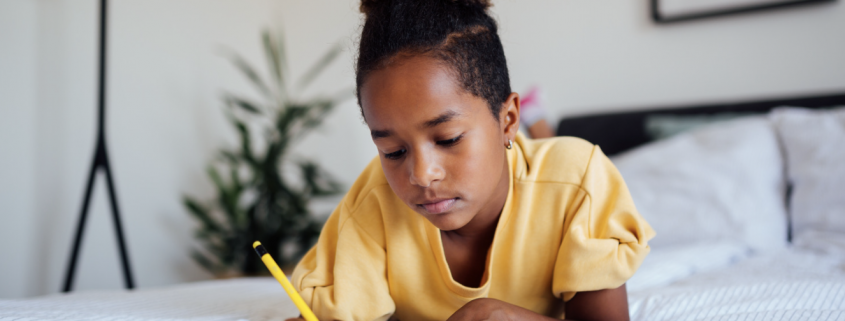 Child doing homework laid on their bed.