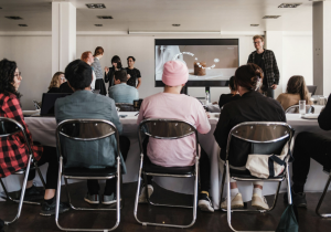 Adults sat around a table looking at a speaker at a conference. 