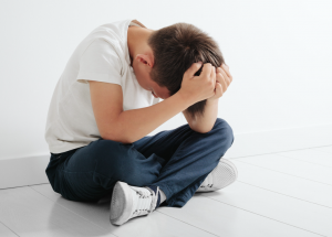 young boy sat on the floor holding his head in his hands. 