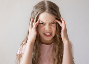 A white girl with long hair holding her temples and pulling a grimace face. 