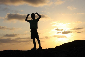 a boy in silhouette holding his arms up in celebration