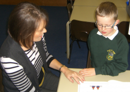 Teaching assistant sharing a story with a boy pupil in a green jumper.