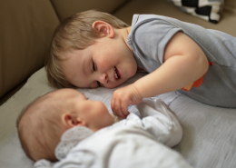young boy lying next to a baby holding it's hand.