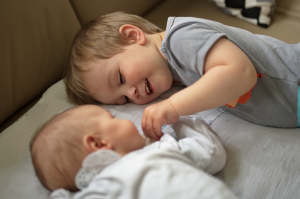 young boy lying next to a baby holding it's hand. 