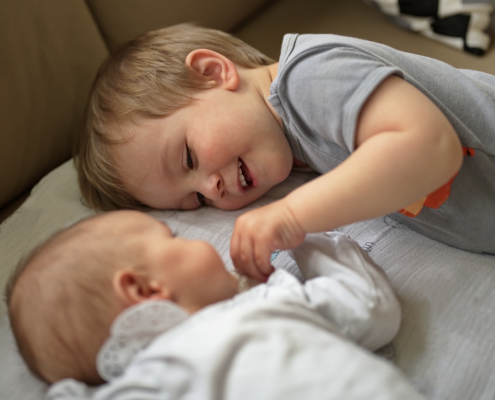 young boy lying next to a baby holding it's hand.