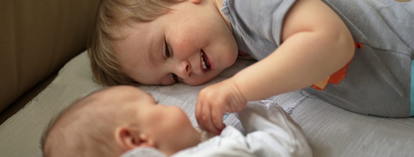 young boy lying next to a baby holding it's hand.