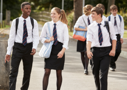 A group of 3 secondary school students walking across a school yard.