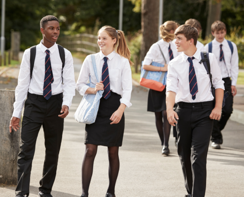 A group of 3 secondary school students walking across a school yard.