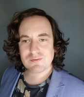 white male with wavy shoulder length hair and pale blue jacket