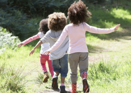 three young children following each other down a grassy path. You only seethe back of them.