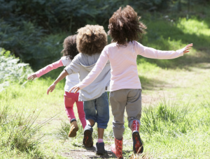 three young children following each other down a grassy path. You only seethe back of them.