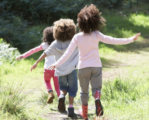 three young children following each other down a grassy path. You only seethe back of them.